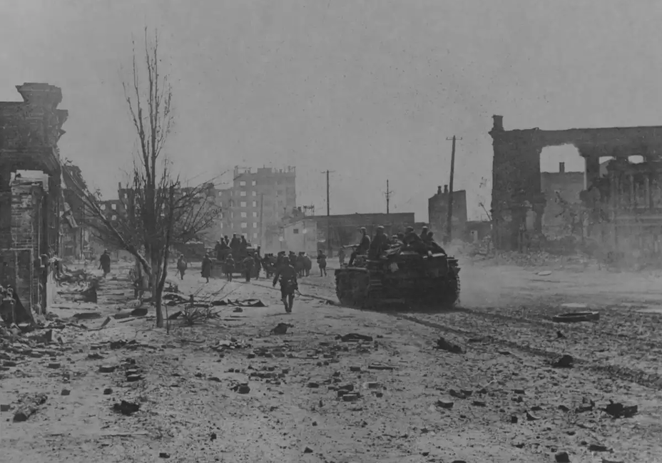 ​Stugs from the 244th Division (Sturmgeschütz Abteilung) with infantry from 194th Infantry Regiment on Kurskaya street. The vehicles are loaded with boxes of ammunition, next to them are prisoners of war «khivi» with a trench tool. The «house of specialists» is visible in the distance - Unknown Stalingrad: Enemy at the Gates | Warspot.net